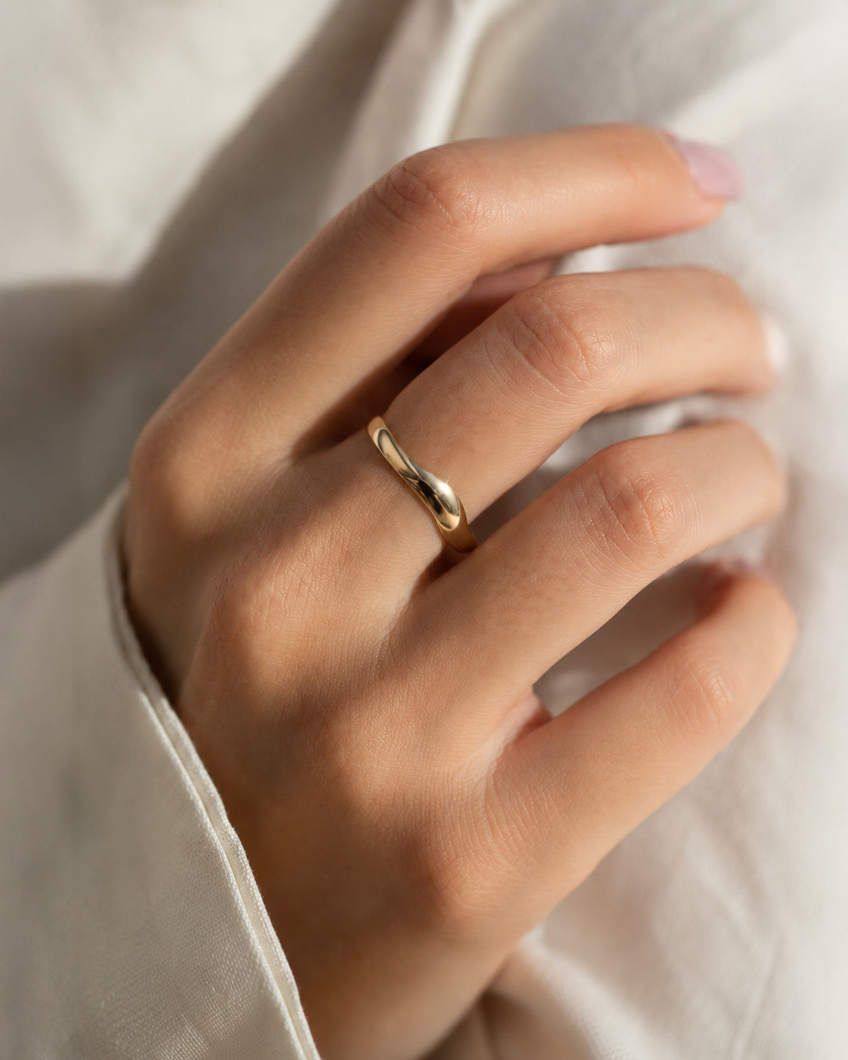 Sway Ring in yellow gold worn on a finger, a smooth band with a gentle wave