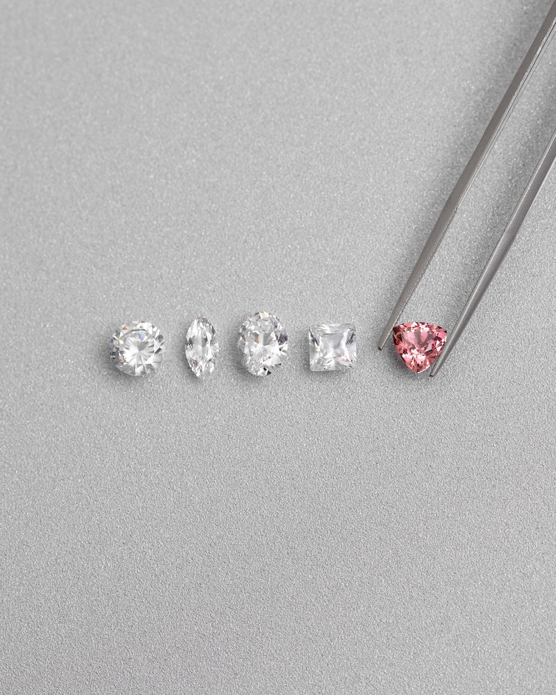 Assorted diamond shapes including round, oval, marquise, princess and pink trillion held with tweezers by William Edouard