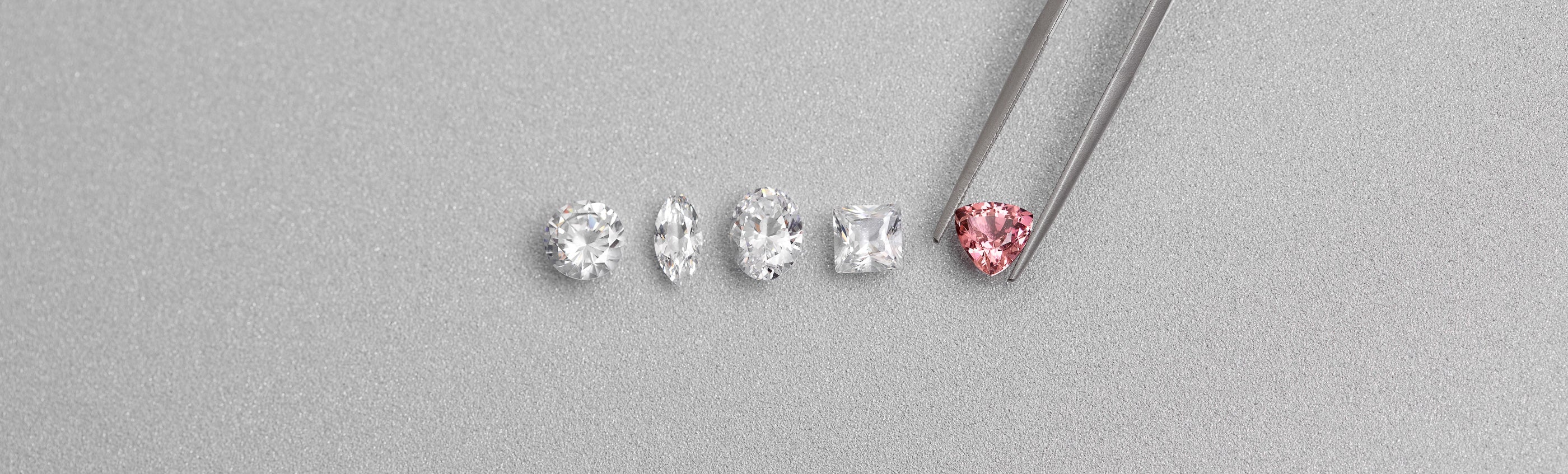 Assorted diamond shapes including round, oval, marquise, princess and pink trillion held with tweezers by William Edouard