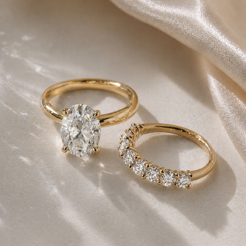Oval diamond engagement ring in yellow gold paired with curved diamond wedding band by William Edouard