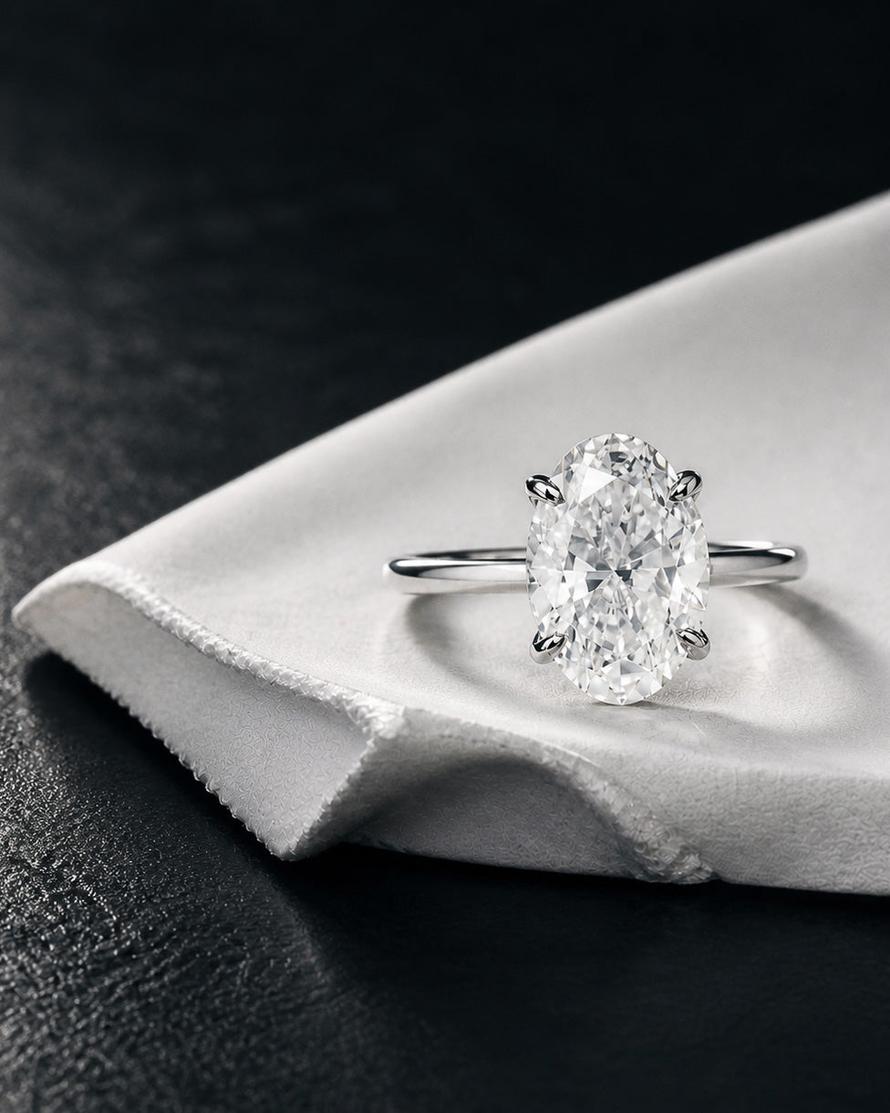 Oval diamond solitaire engagement ring with four prong setting in white gold by William Edouard on fabric