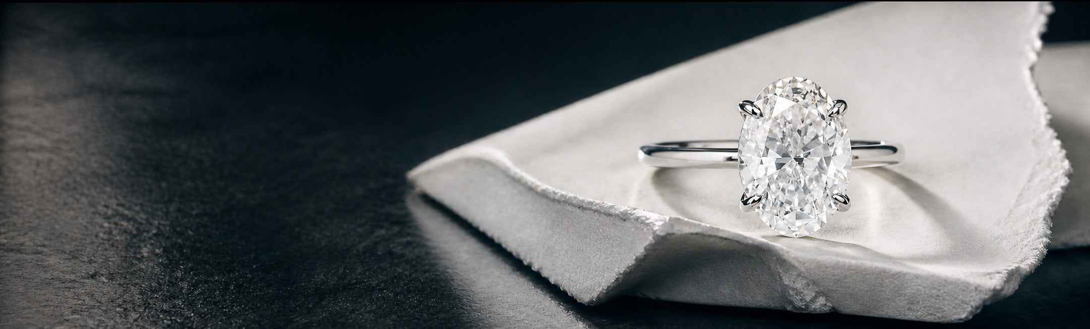 Oval diamond solitaire engagement ring with four prong setting in white gold by William Edouard on fabric