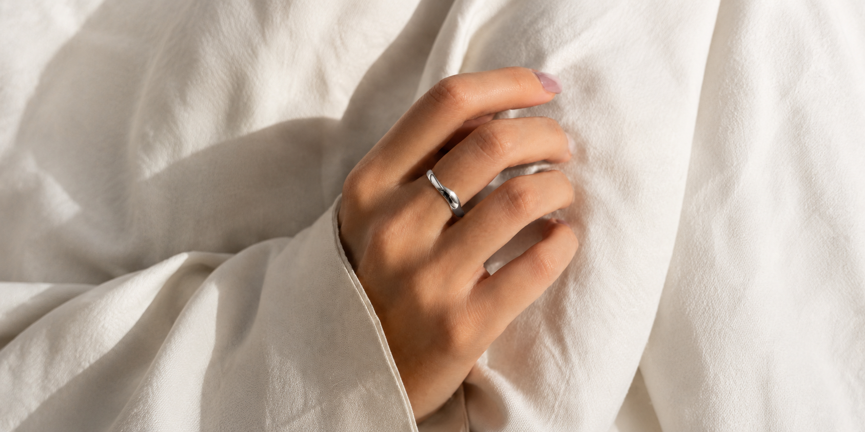 Minimalist silver wave band ring on hand with soft bridal styling by William Edouard