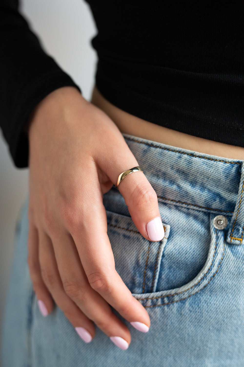 Sway Ring in yellow gold worn on a finger of a hand resting at the hip